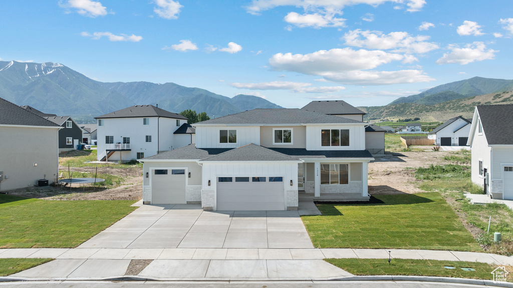 View of front of home with an attached garage, a mountain view, driveway, and a front lawn