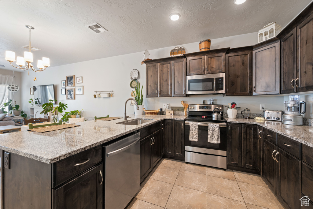 Kitchen featuring stainless steel appliances, a peninsula, light tile patterned flooring, light stone countertops, and a chandelier