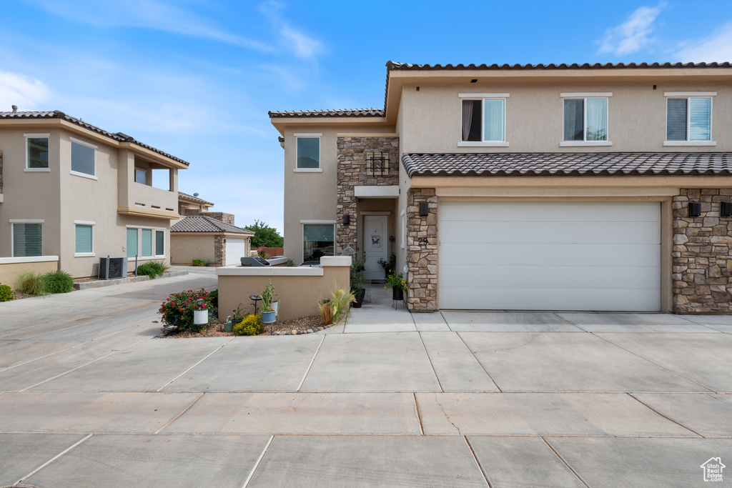 Multi unit property with stone siding, driveway, stucco siding, a tiled roof, and an attached garage