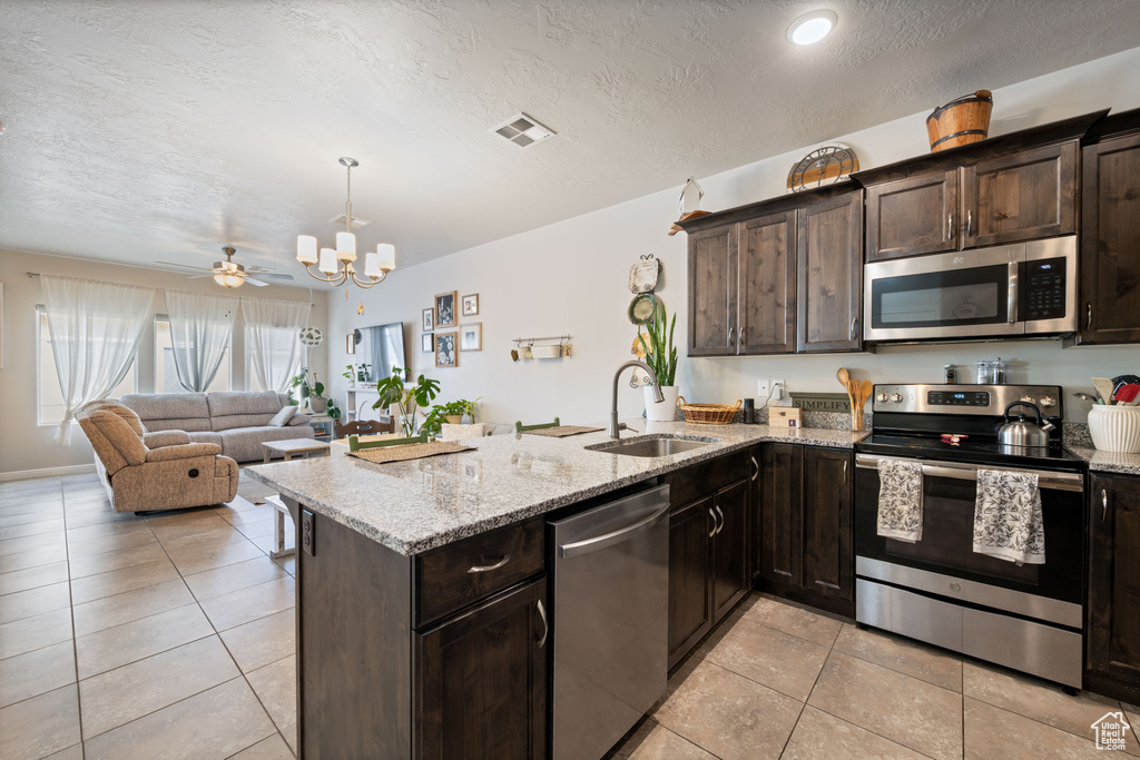 Kitchen with appliances with stainless steel finishes, dark brown cabinets, a peninsula, light tile patterned floors, and a chandelier