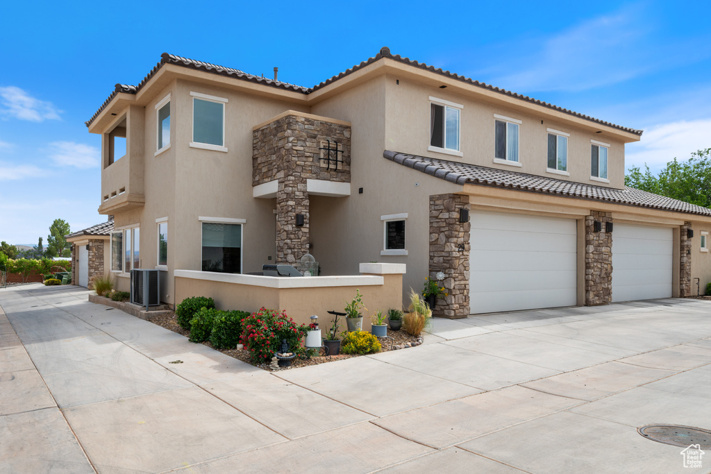 View of front of property featuring stucco siding, stone siding, a tiled roof, driveway, and a garage