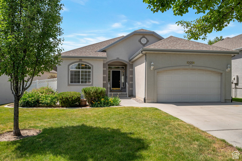View of front of home with stucco siding, a garage, driveway, and roof with shingles