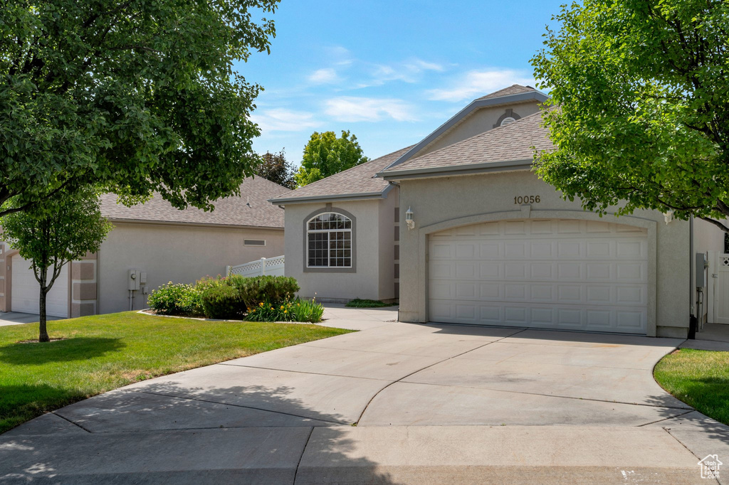 View of front of house featuring stucco siding, driveway, a front lawn, a garage, and a shingled roof