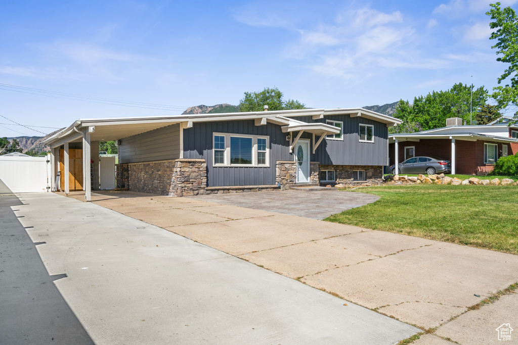 View of front facade featuring concrete driveway, stone siding, an attached carport, and a gate