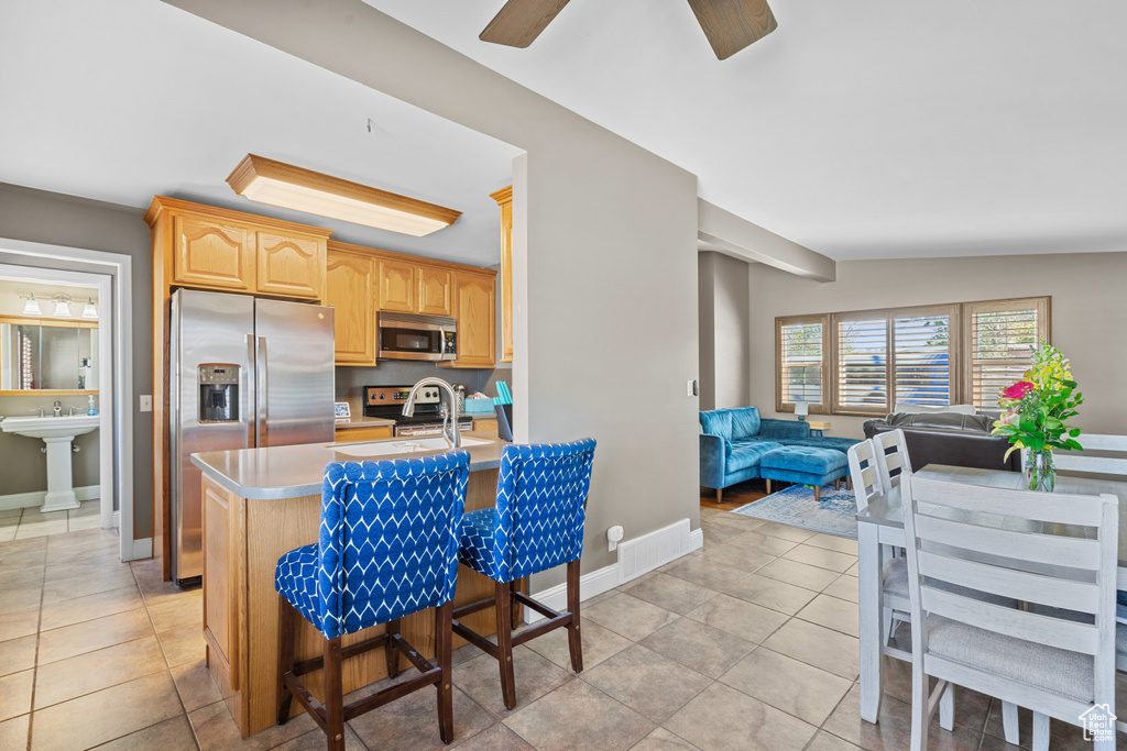 Kitchen featuring stainless steel appliances, open floor plan, light countertops, light tile patterned floors, and a kitchen breakfast bar