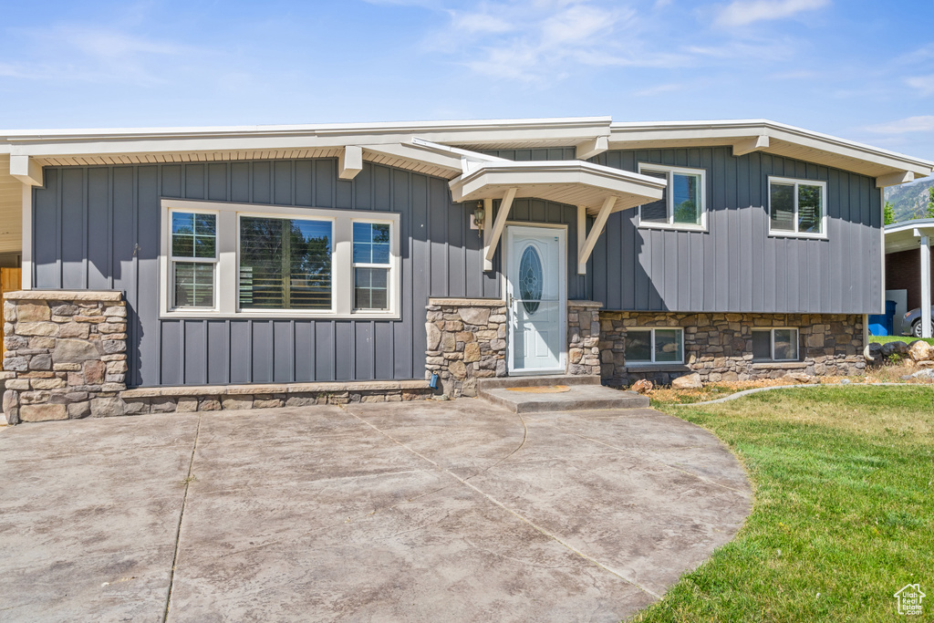 View of front of property featuring board and batten siding, a front yard, and stone siding