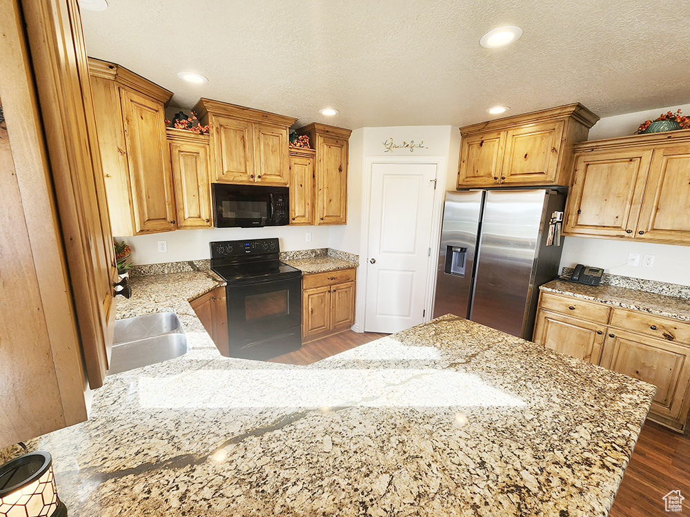 Kitchen with black appliances, a peninsula, dark wood-style flooring, light stone counters, and recessed lighting