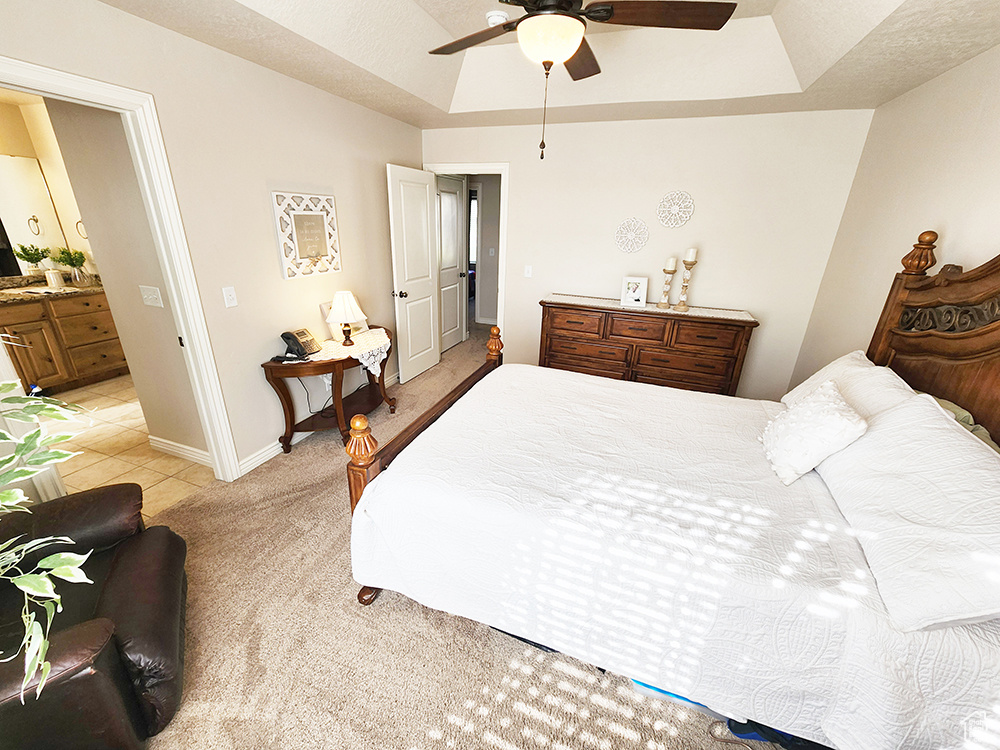 Bedroom with a tray ceiling, light carpet, ensuite bathroom, and a ceiling fan