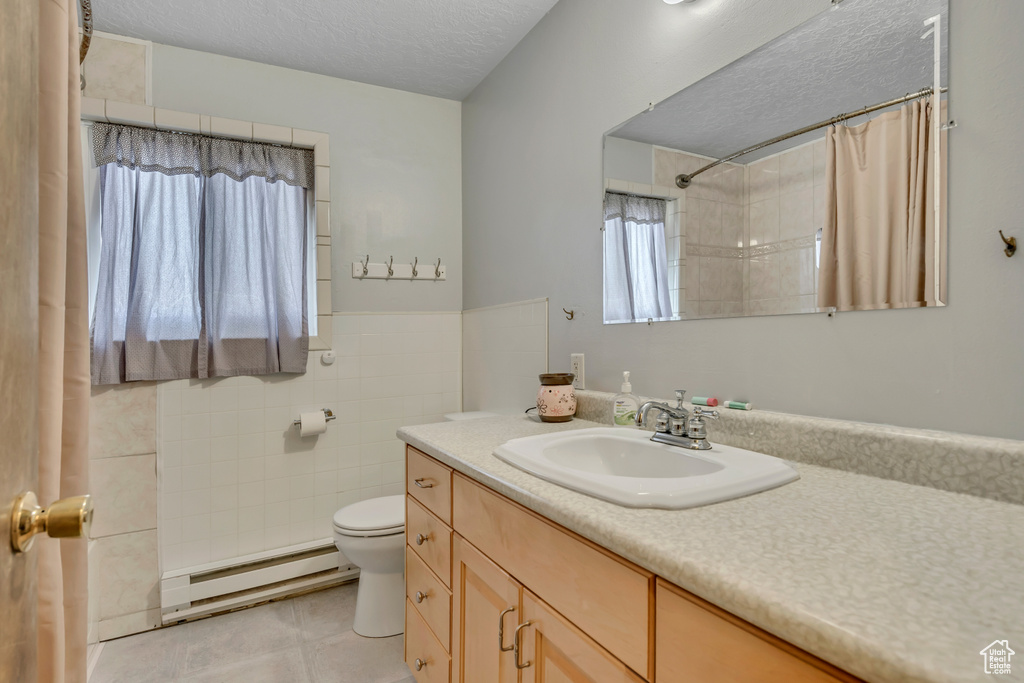 Full bathroom with baseboard heating, vanity, a textured ceiling, a shower with shower curtain, and tile patterned flooring