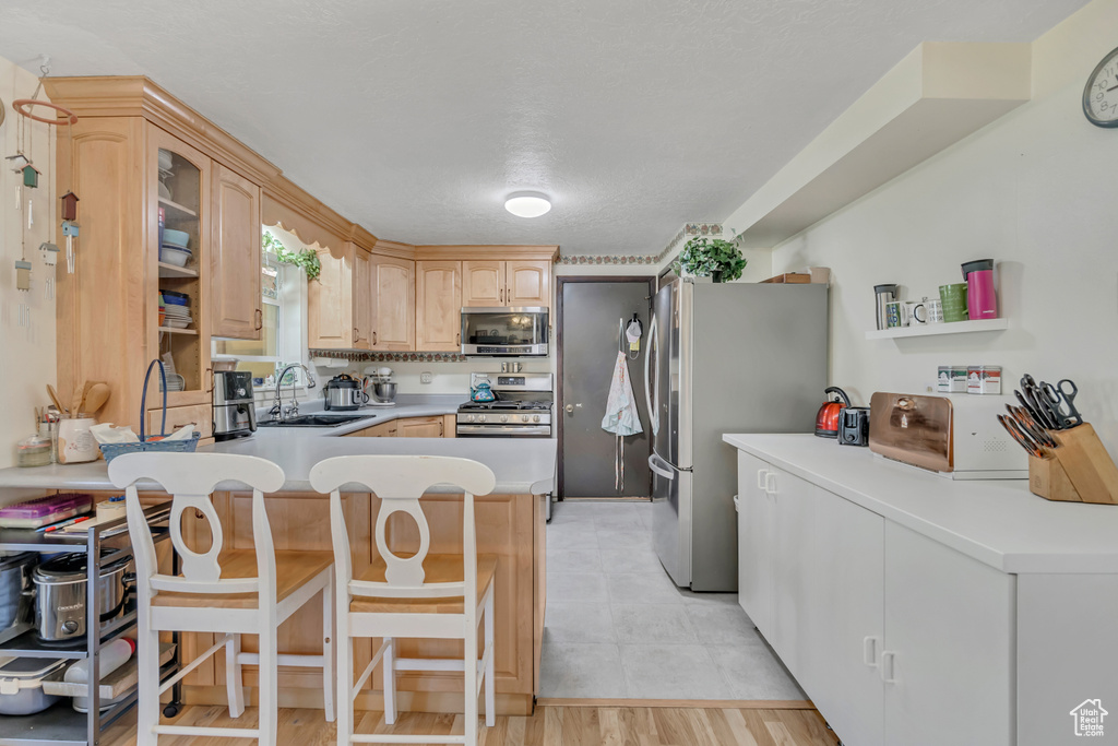 Kitchen featuring appliances with stainless steel finishes, a peninsula, light brown cabinetry, a breakfast bar, and light countertops