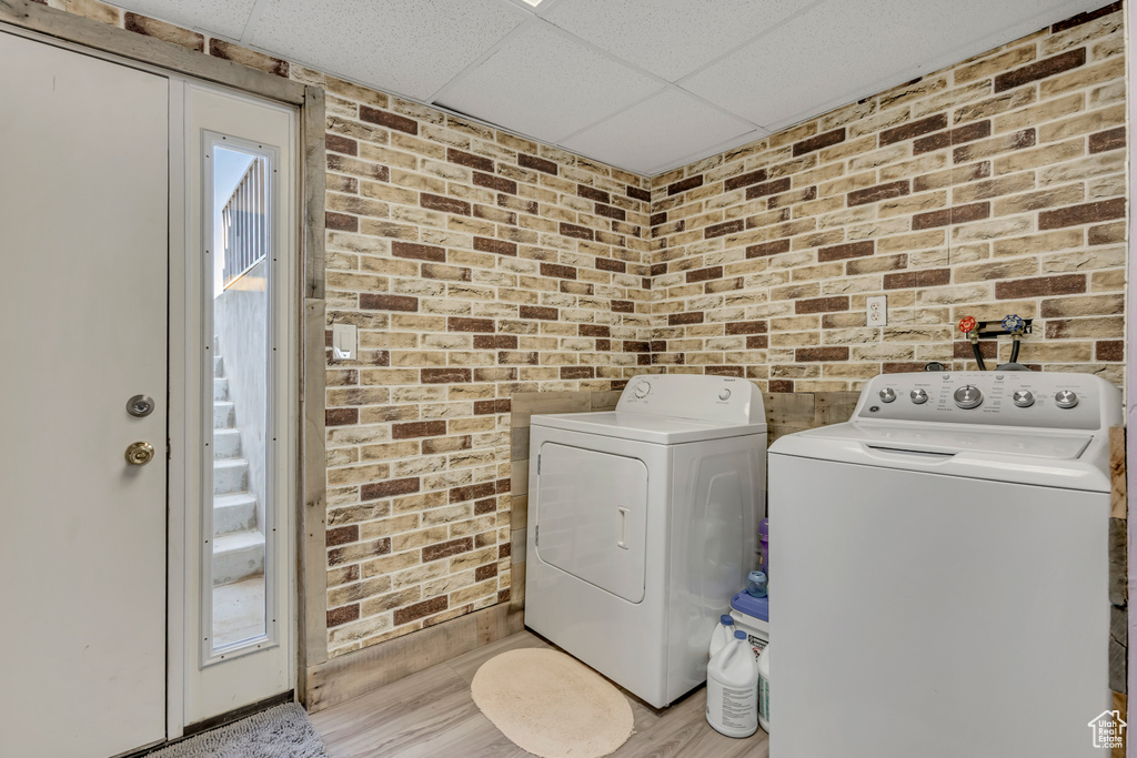 Laundry area with independent washer and dryer, brick wall, and light wood finished floors