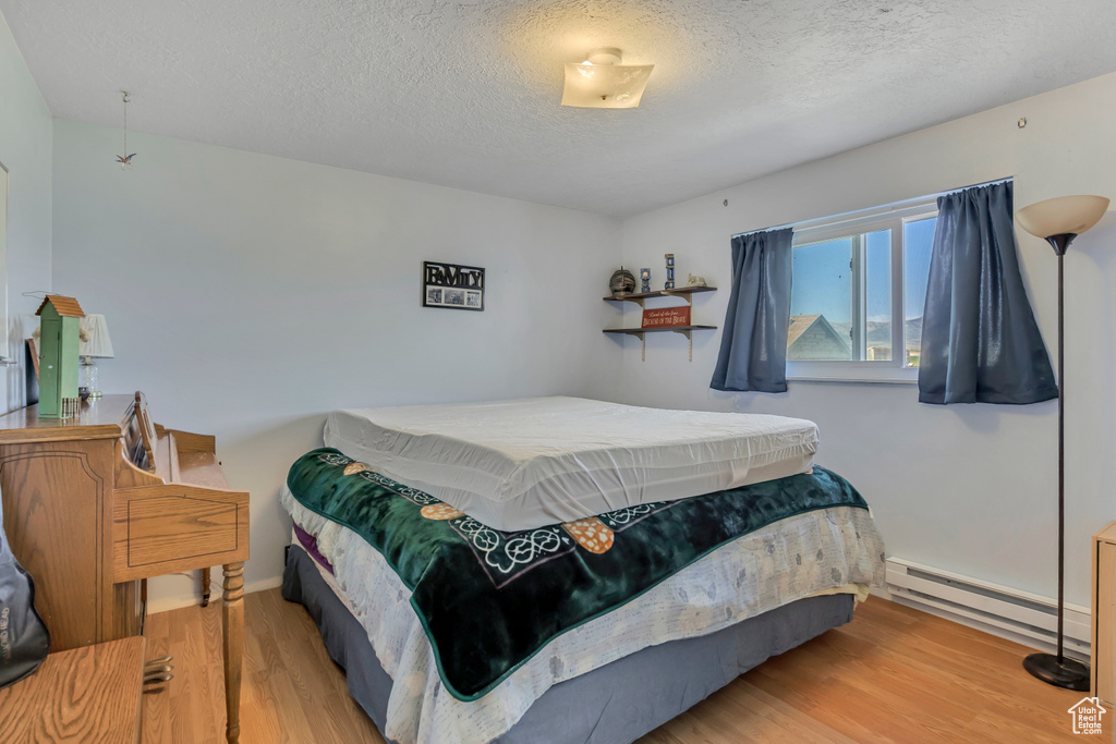 Bedroom with a baseboard radiator, wood finished floors, and a textured ceiling