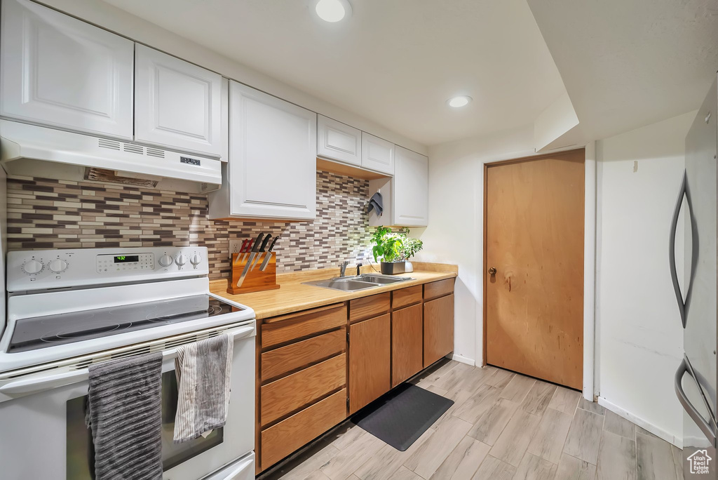 Kitchen featuring white electric range oven, under cabinet range hood, light countertops, white cabinetry, and backsplash