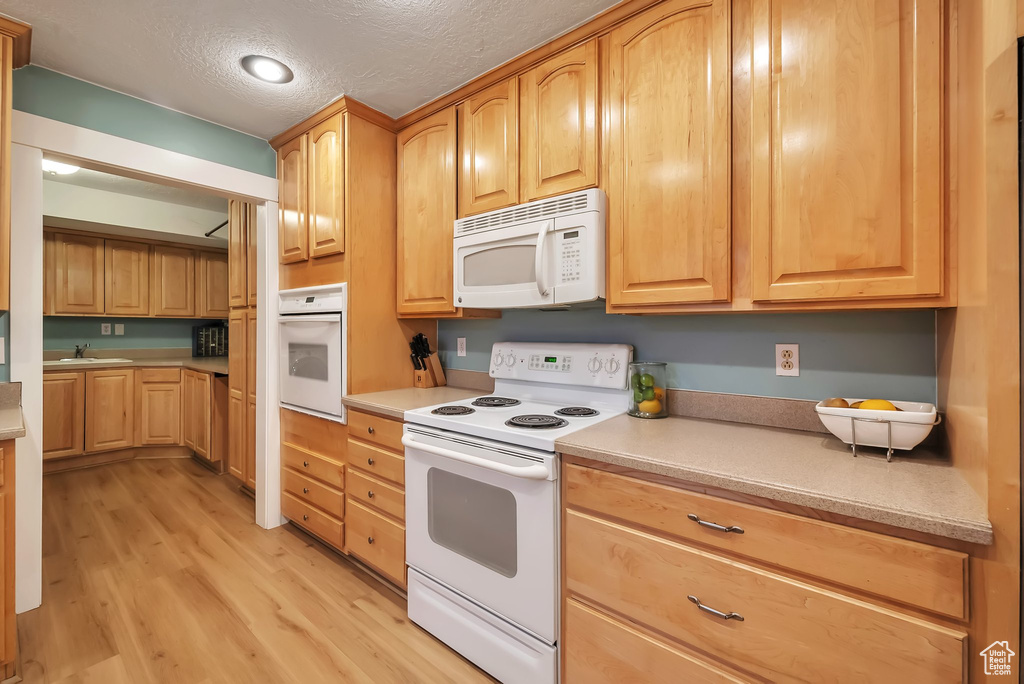 Kitchen with white appliances, light wood-style flooring, a textured ceiling, light countertops, and light brown cabinets
