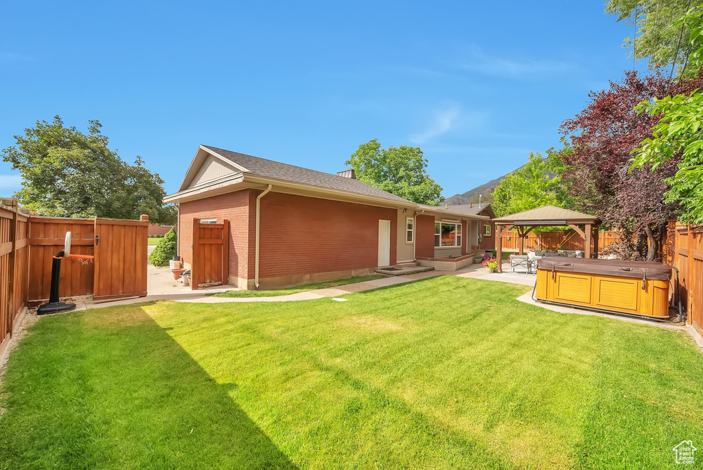 Rear view of house featuring a hot tub, a fenced backyard, brick siding, a patio, and a gazebo