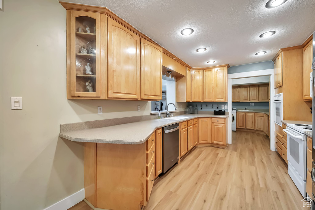 Kitchen with white appliances, light wood-type flooring, glass insert cabinets, a textured ceiling, and washer / clothes dryer
