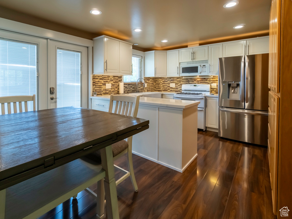 Kitchen featuring white appliances, dark wood-style floors, light countertops, tasteful backsplash, and white cabinets