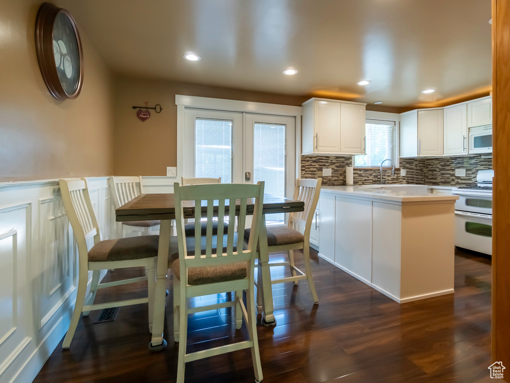 Dining room featuring dark wood-type flooring, a decorative wall, french doors, wainscoting, and recessed lighting