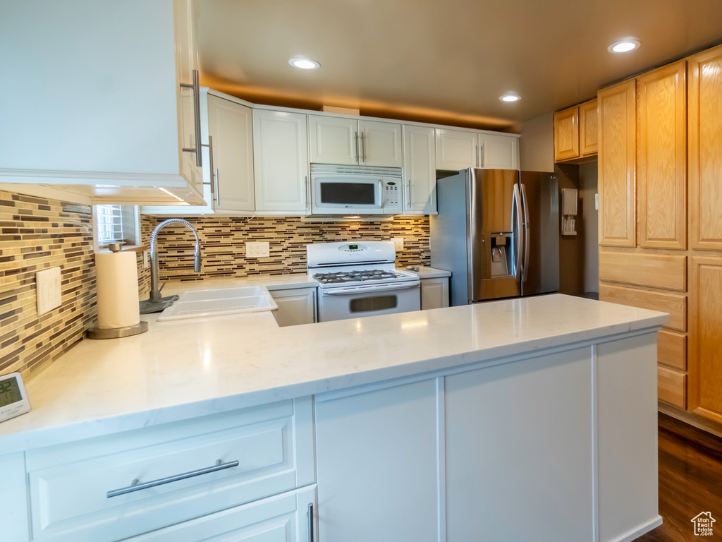 Kitchen featuring white appliances, decorative backsplash, recessed lighting, a peninsula, and light stone counters