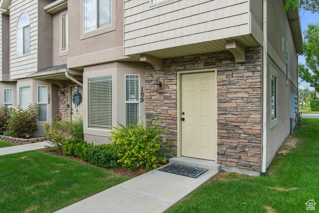 Property entrance with stone siding, a lawn, and stucco siding