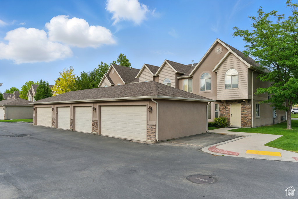 View of property with stone siding, community garages, roof with shingles, and stucco siding