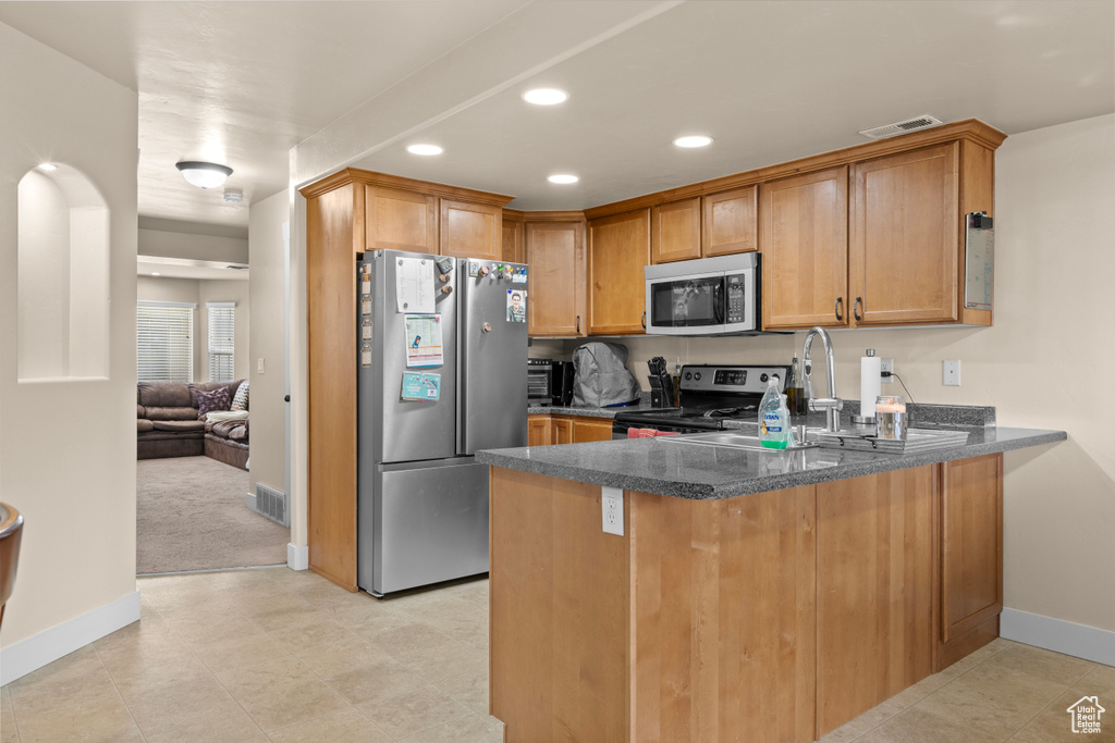 Kitchen with stainless steel appliances, a peninsula, recessed lighting, brown cabinets, and dark stone counters