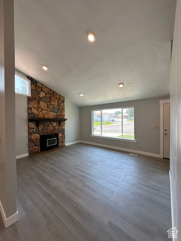 Unfurnished living room featuring a textured ceiling, lofted ceiling, wood finished floors, and a fireplace