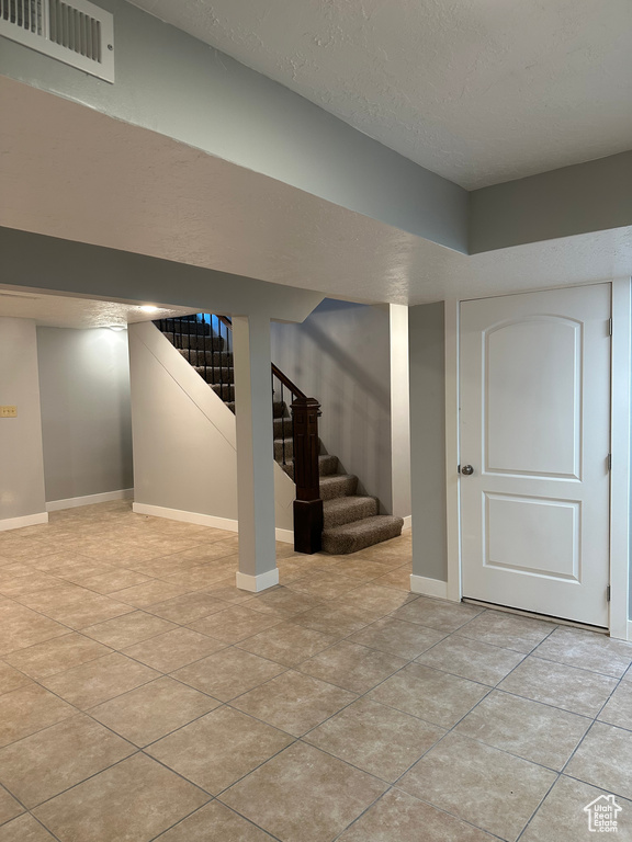 Finished below grade area featuring stairs, light tile patterned floors, and a textured ceiling