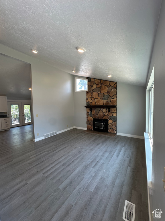 Unfurnished living room with a textured ceiling, dark wood-style flooring, plenty of natural light, a stone fireplace, and french doors