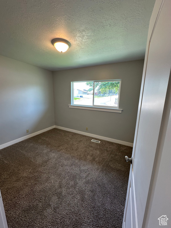 Unfurnished room featuring a textured ceiling and dark carpet