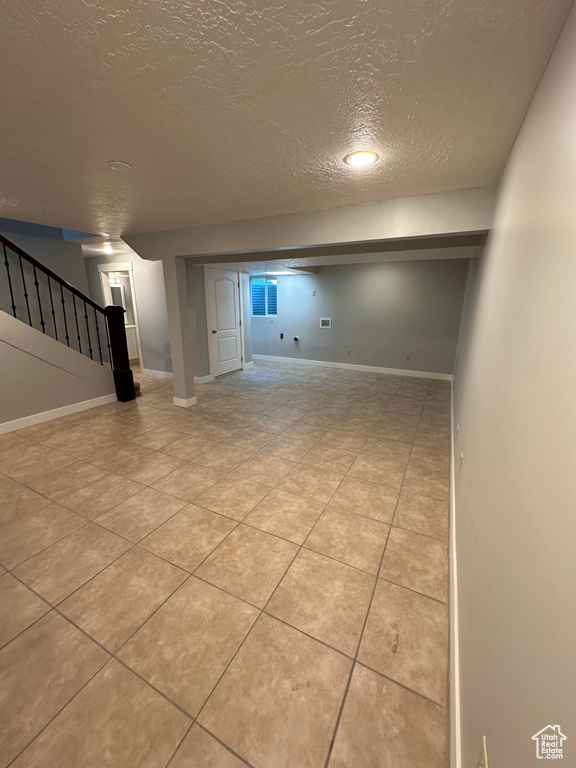 Finished below grade area with a textured ceiling, stairs, and light tile patterned floors