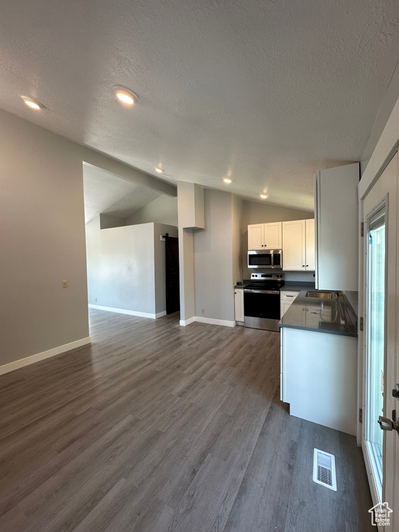 Kitchen with appliances with stainless steel finishes, a textured ceiling, dark countertops, lofted ceiling, and dark wood-style floors