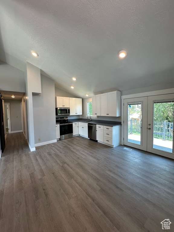 Kitchen with stainless steel appliances, vaulted ceiling, dark countertops, plenty of natural light, and white cabinetry