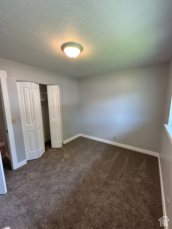 Unfurnished bedroom with a textured ceiling, dark carpet, and a closet