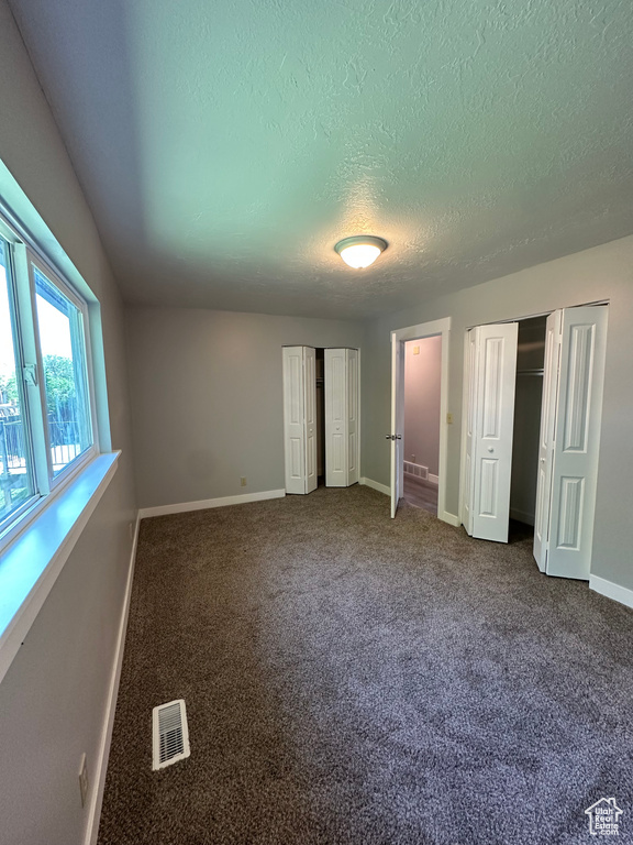 Unfurnished bedroom with multiple closets, a textured ceiling, and carpet floors