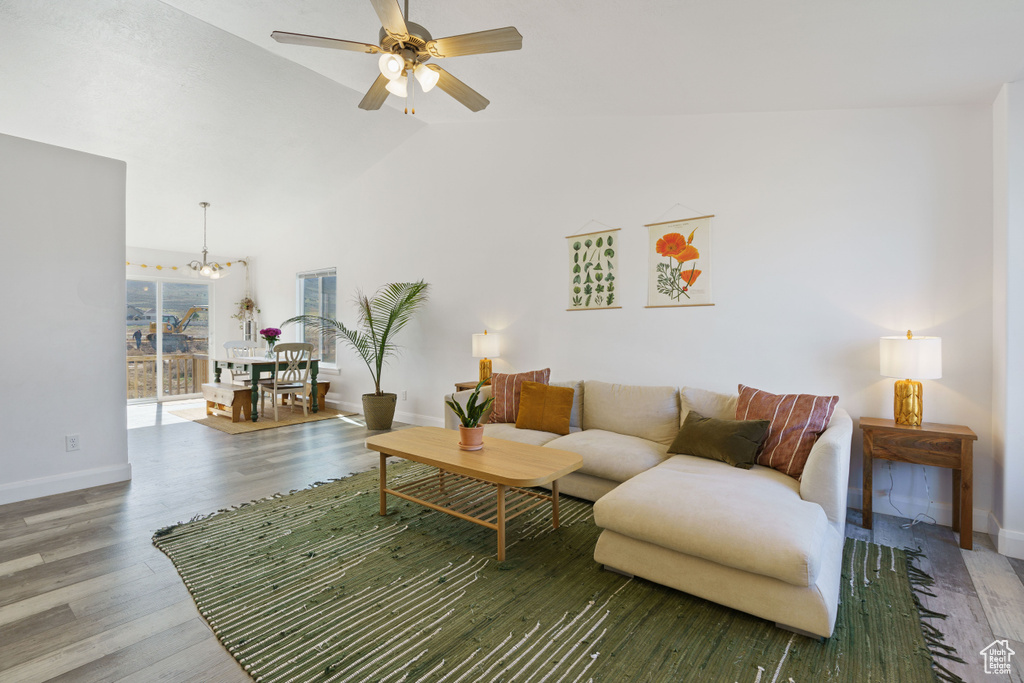 Living room featuring a chandelier, ceiling fan, lofted ceiling, wood finished floors, and baseboards