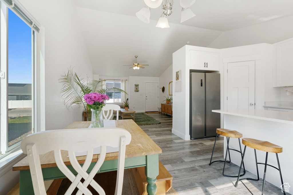 Kitchen with freestanding refrigerator, a ceiling fan, lofted ceiling, light wood-style floors, and a kitchen breakfast bar