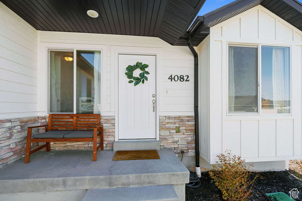 Property entrance with board and batten siding, stone siding, and a porch