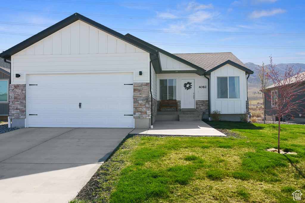 View of front facade featuring board and batten siding, a front yard, a garage, concrete driveway, and stone siding