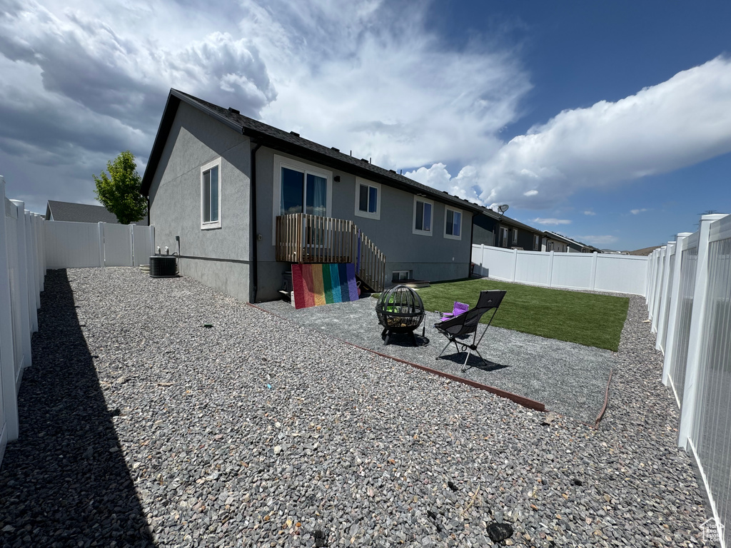 Back of house with an outdoor fire pit, stucco siding, and central AC