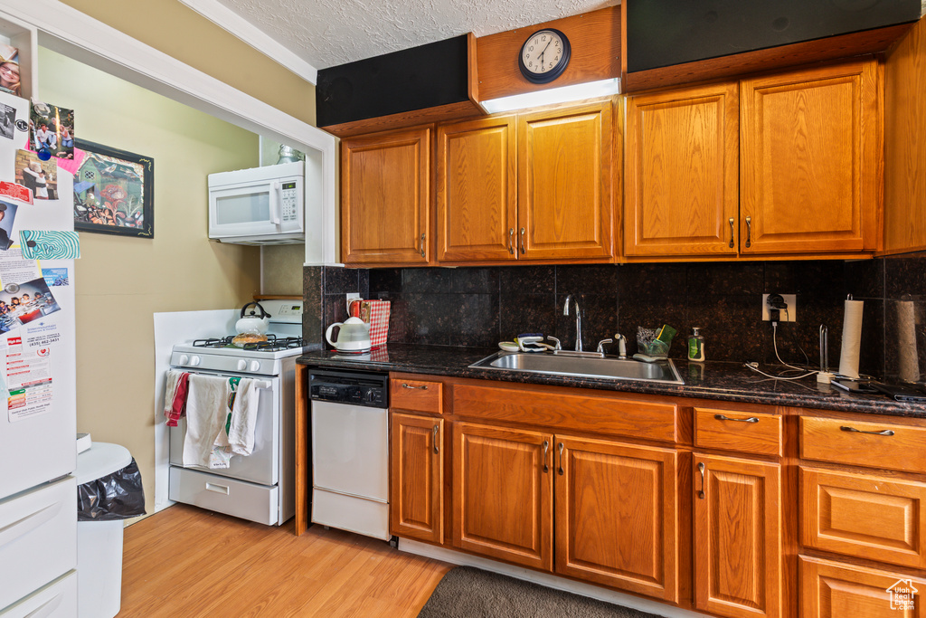 Kitchen featuring white appliances, brown cabinets, light wood-style flooring, and a textured ceiling