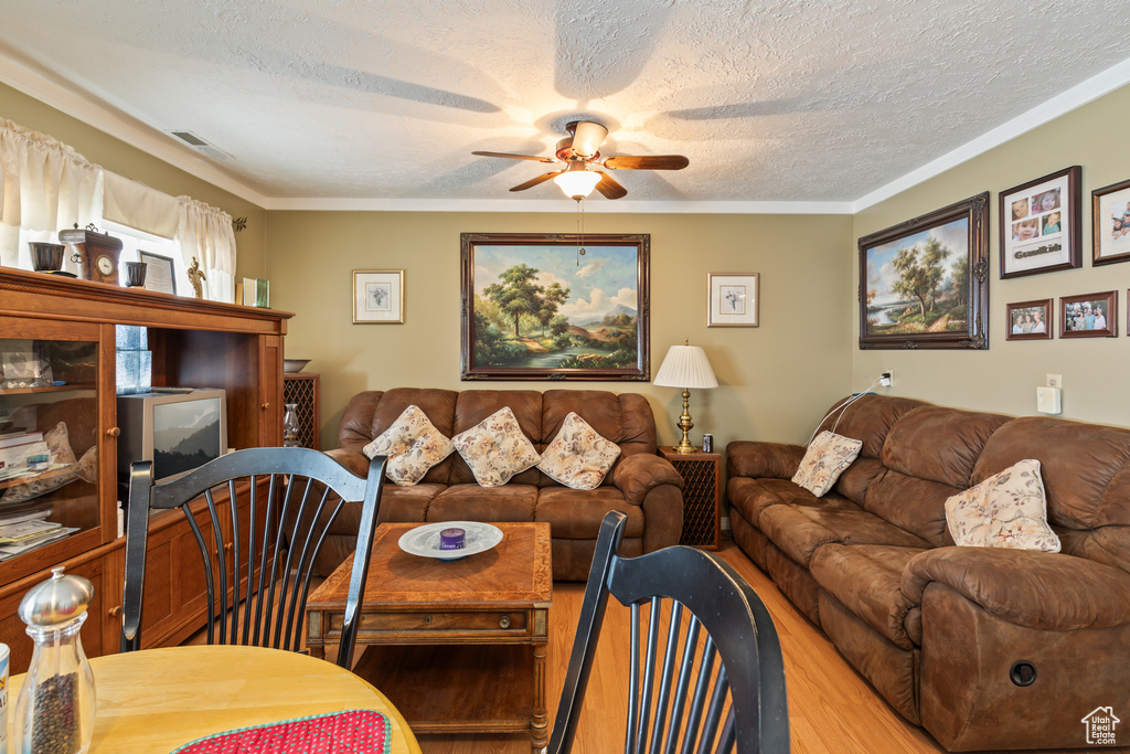 Living room with a textured ceiling, ceiling fan, wood finished floors, and ornamental molding