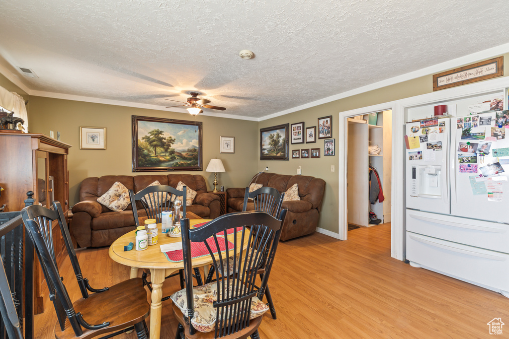 Dining area with ceiling fan, a textured ceiling, light wood-type flooring, and crown molding