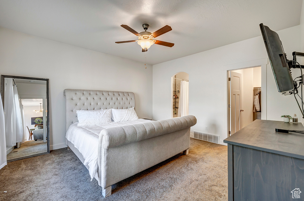 Bedroom with light colored carpet, arched walkways, and ceiling fan