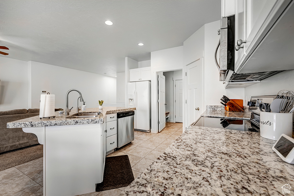 Kitchen with stainless steel appliances, open floor plan, white cabinets, light tile patterned floors, and a kitchen island with sink