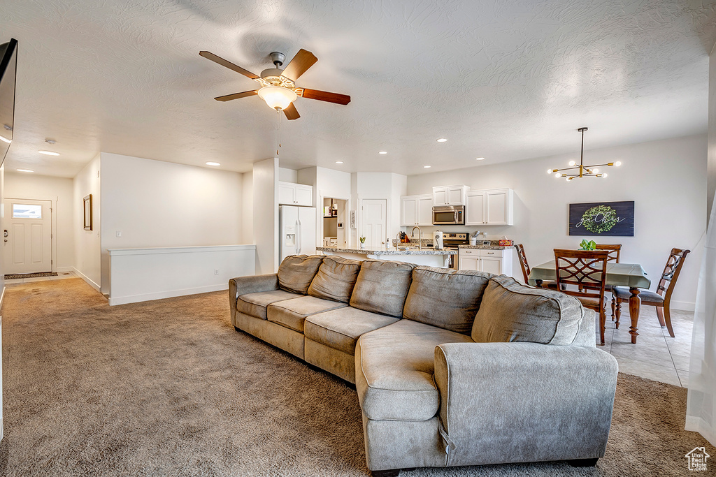 Living room featuring light colored carpet, a chandelier, a ceiling fan, recessed lighting, and a textured ceiling