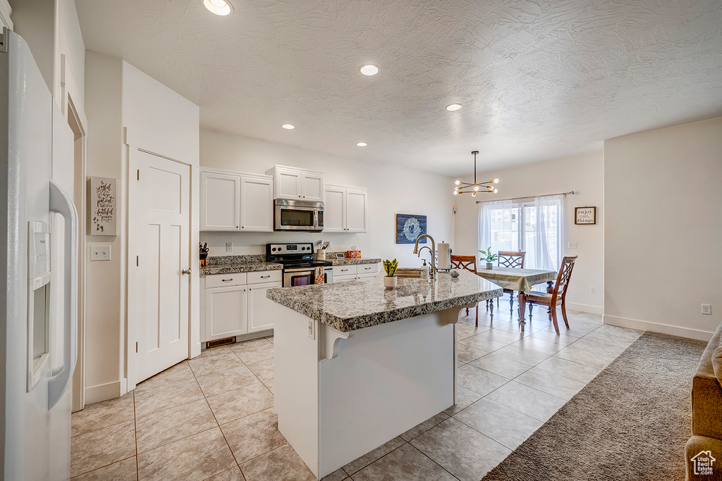 Kitchen with stainless steel appliances, a chandelier, recessed lighting, white cabinets, and an island with sink
