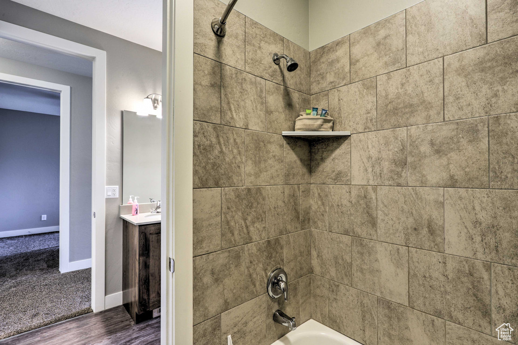 Bathroom view of  shower combination, wood finished floors, vanity, and baseboards