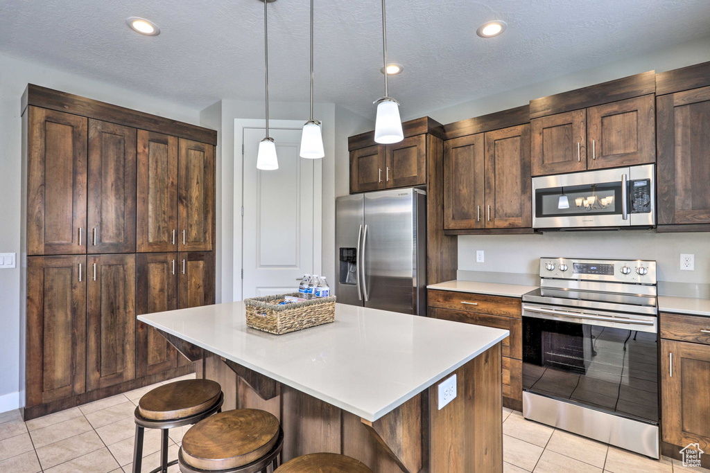 Kitchen featuring stainless steel appliances, a kitchen bar, light countertops, light tile patterned floors, and a center island
