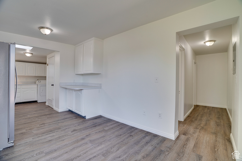Kitchen featuring washer / clothes dryer, freestanding refrigerator, light wood finished floors, white cabinetry, and light countertops